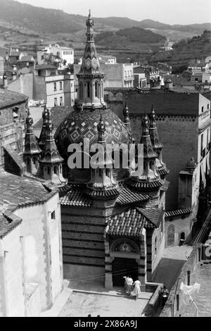 Die mit bunten Mosaiksteinen besetzten Kuppeln der Pfarrkirche von Sant Romà, dem Schutzpatron der Stadt, durch die Kirchentür betreten Frauen das Gotteshaus rechtzeitig zum Gottesdienst, Lloret de Mar 1957. Die Kuppeln der Pfarrkirche von Sant Romà, dem Schutzpatron der Stadt, sind mit bunten Mosaiksteinen verziert; Frauen betreten die Kirche rechtzeitig zum Gottesdienst, Lloret de Mar 1957. Stockfoto