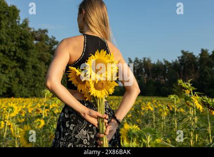 Unerkennbare blonde Frau, die einen Blumenstrauß hinter ihrem Rücken hält Stockfoto