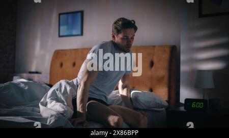 Der Mann wacht auf, schaltet den Wecker vor Frustration aus, nach einer schlaflosen Insomniac-Nacht. Gestresster Mann, bereit für den Tag der Problemlösung. Uhr zeigt sechs Uhr MORGENS Schlafzimmer Nachttisch Schlafzimmer Stockfoto