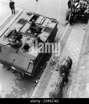 Ein Geschäftsmann zieht einen voll-behängten Geraderobenständer vor einem Panzer der US-Army über den Bürgersteig. Im Hintergrund haben sich interessierte Passantinnen und Passanten zahlreich auf den Bürgersteigen versammelt, Berlin 1961. - Originale Bildbeschreibung: "Die Damenoberbekleidung arbeitet unter den Augen von amerikanischen Soldaten. Trotz der gespannten Situation geht die Arbeit der West-Berliner wie immer voran. - Übergriffe werden abgewiesen - zu einem schweren Grenzzwischenfall kam es auch heute wieder an der Friedrich-/Ecke Kochstraße, als zwei amerikanische Reiseomnibussen Stockfoto