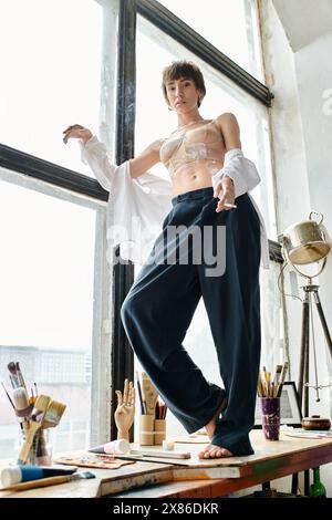 Eine Frau steht selbstbewusst auf einer Fensterbank, mit Silhouette vor einem Fenster. Stockfoto