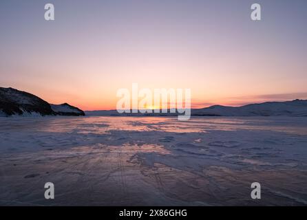 Das schneebedeckte Eis des Baikalsees und der felsigen Insel. Winterlandschaft des gefrorenen Baikals bei schönem Sonnenaufgang in Flieder. Sonnenreflexionen auf dem Eis Stockfoto