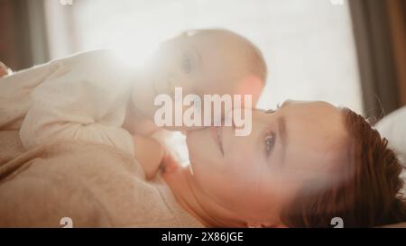 Liebende junge, liebevolle Mutter, die zu Hause ein entzückendes Baby spielt und pflegt. Lächelnde schöne Mutter und niedliches kleines Kleinkind kuscheln im Schlafzimmer. Mütterliche Zärtlichkeiten. Stockfoto