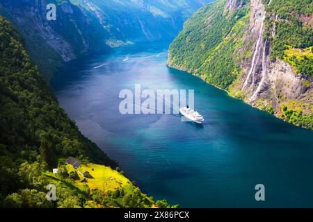 Ein großes Kreuzfahrtschiff im klaren azurblauen Wasser des Fjords Sunnylvsfjorden in der Nähe des Dorfes Geiranger in Westnorwegen. Berühmte Wasserfälle der sieben Schwestern im Hintergrund Stockfoto