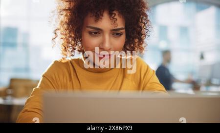 Low Angle Porträt einer ausdrucksstarken, multiethnischen arabischen Frau, die an einer kreativen Stelle in einer Werbefirma arbeitet. Konzentrierter Manager kommuniziert mit Kollegen und schreibt einen Geschäftsplan. Stockfoto