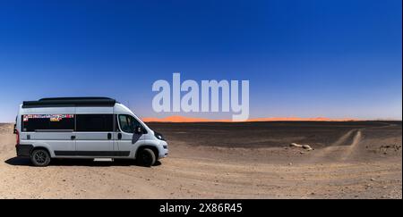 Merzouga, Marokko - 8. März 2024: Gut gereister Wohnmobil parkt in einer einsamen Landschaft mit orangen Sanddünen und schwarzer Felsenwüste im Südosten Stockfoto