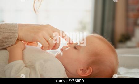 Nahaufnahme Porträt einer liebevollen jungen schönen Mutter, die liebenswertes Baby im Bett spielt und beruhigt. Lächelnde, fürsorgliche Mutter und niedliches kleines Kind, das im Schlafzimmer kuschelt. Mütterliche Zärtlichkeiten. Stockfoto