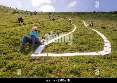 Wilmington, East Sussex, Großbritannien, 23.05.2024, Freiwillige Linda Miles helfen, den langen Mann von Wilmington zu malen. Die Riesenfigur an den steilen Hängen des Windover Hill ist 72 Meter hoch und hält zwei Stangen. Ursprünglich wurde angenommen, dass es sich um ein neolithikum handelt, heute wird angenommen, dass es sich um das 16. Oder 17. Jahrhundert handelt. Die Neumalerei ist das Finale einer Spendenaktion zur Unterstützung der Arbeit der Sussex Archaeology Society (die als Sussex Past gehandelt wird), die die berühmte Hügelfigur „The Guardian of the South Downs“ besitzt und pflegt. Die Kampagne sammelte mehr als £10.000 und fast 300 Spender zahlten £30,00 für die Adoption Stockfoto