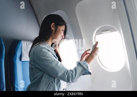 Hipster-Reisende, die während der Sommerferien in einem Passagierflugzeug einen Blick auf das Fenster machen. Das Konzept, Momente während des Fluges festzuhalten Stockfoto