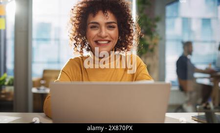 Porträt einer attraktiven arabischen Frau in Kreativagentur. Junger, stylischer Manager mit lockigem Haar, der die Kamera ansieht. Manager, der in einem modernen Unternehmen arbeitet. Stockfoto