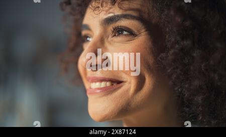 Nahaufnahme Porträt einer multiethnischen Brünette mit lockigen Haaren und braunen Augen. Fröhliche kreative junge Frau, die charmant lächelt und sich fröhlich fühlt. Gedanken Über Eine Größere Zukunft. Stockfoto