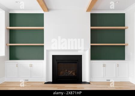 Ein Kamin mit eingebauten Regalen aus weißer Eiche, weißen Eichenböden und -Balken, grünen Akzenten und weißem Marmor umgeben den Kamin. Stockfoto