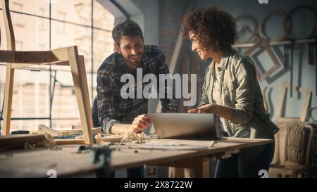 Junge Mann und Frau, die Laptop benutzen, über ein erfolgreiches Projekt in einem Zimmermannsstudio diskutieren. Möbeldesigner High Five und feiern, dass sie eine große Geschäftschance erhalten. Stockfoto