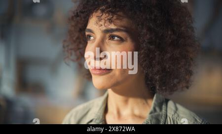 Nahaufnahme Porträt einer dunkelhäutigen, multiethnischen Brünette mit lockigen Haaren und braunen Augen. Glückliche kreative junge Frau, die in die Kamera blickt und charmant lächelt. Stockfoto