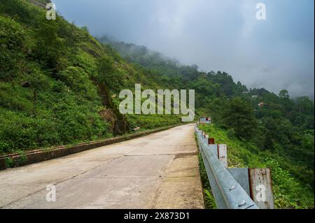 Betonstraße, die durch die Berge des Himalaya und den üppigen grünen Wald führt. Landschaftlich schöne Monsunlandschaft in Darjeeling, Westbengalen, Indien. Stockfoto