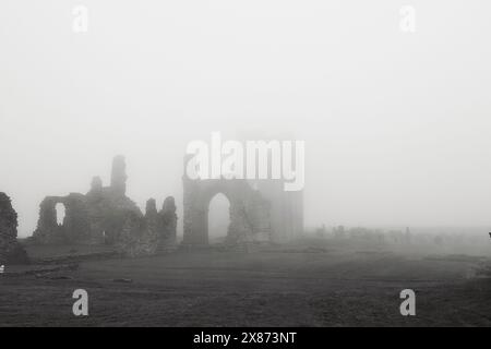 Eine nebelige Landschaft mit den Ruinen eines alten Steingebäudes, mit Bögen und Mauern, die teilweise durch den dichten Nebel sichtbar sind. Die Szene ist unheimlich Stockfoto