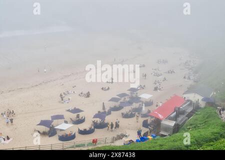 Eine neblige Strandszene mit Leuten, die sich unter Sonnenschirmen und in der Nähe eines Food Trucks entspannen. Stockfoto