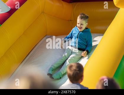 Junge rutscht auf einer aufblasbaren Seite herunter. Das Konzept eines Kindes im Sommer auf einem Trampolin. Stockfoto