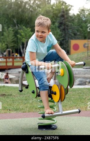 Ein glückliches Kind reitet auf einer grünen Grashüpfer-Federschaukel auf einem städtischen Kinderspielplatz. Stockfoto