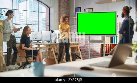 Positive Geschäftsfrau, die ein Team-Meeting im Konferenzraum „Creative Office“ leitet. Aufgeregte multiethnische Frau zeigt Präsentation auf Green Screen Mock Up Chroma Key Monitor. Stockfoto