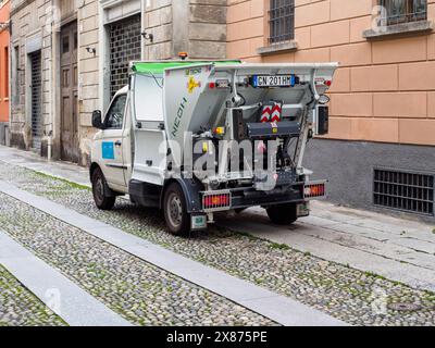 Cremona, Italien - 5. Mai 2024, kleiner weißer Müllwagen, der für die Abfallentsorgung in der Stadt ausgerüstet ist, parkt auf einer Kopfsteinpflasterstraße neben Gebäuden Stockfoto