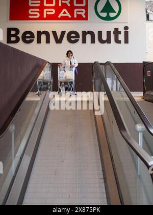 Cremona, Italien - 5. Mai 2024, Käuferinnen stehen auf einer Rolltreppe mit vollem Einkaufswagen am Eingang eines eurospar-Geschäfts und begrüßen Kunden Stockfoto