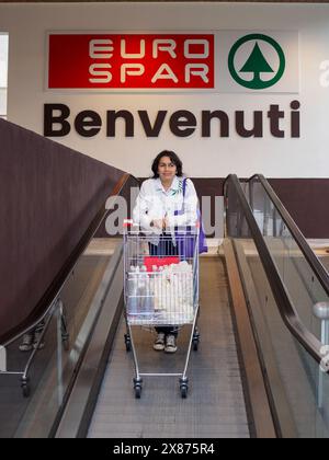 Cremona, Italien - 5. Mai 2024, Käuferinnen stehen auf einer Rolltreppe mit vollem Einkaufswagen am Eingang eines eurospar-Geschäfts und begrüßen Kunden Stockfoto