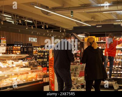 Cremona, Italien - 5. Mai 2024 Junges Paar, das Hände hält, während es in einem Supermarkt durch den Weingang schlendert, umgeben von Regalen mit verschiedenen alkoholischen Be Stockfoto