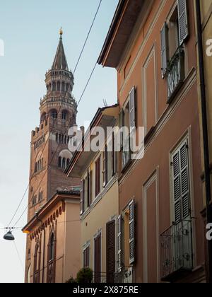 Cremona, Italien - 5. Mai 2024, majestätischer historischer Glockenturm durchsticht den Himmel hinter bezaubernden pastellfarbenen Gebäuden an einer ruhigen europäischen Straßenecke Stockfoto