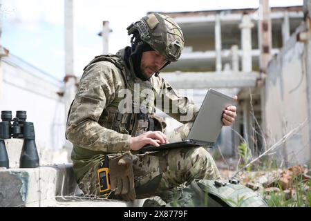 Militärische Mission. Soldat in Uniform mit Laptop in der Nähe eines verlassenen Gebäudes draußen Stockfoto