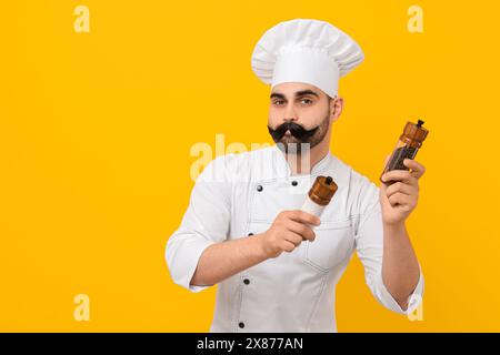 Professioneller Koch mit lustigem künstlichem Schnurrbart, der Shaker auf gelbem Hintergrund hält. Leerzeichen für Text Stockfoto