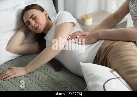 Doula kümmert sich um Schwangere im Schlafzimmer. Vorbereitung auf die Geburt des Kindes Stockfoto