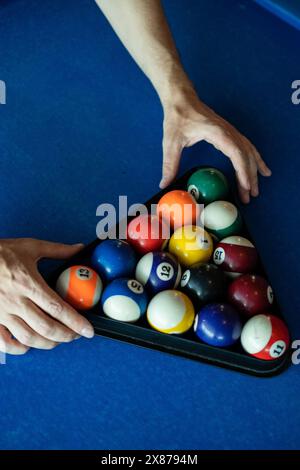 Ein Nahaufnahme-Bild zeigt die Hände, die farbenfrohe Poolbälle in einem dreieckigen Gestell akribisch anordnen Stockfoto