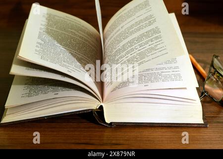 Auf dem Tisch steht ein Buch, das in einem Ventilator geöffnet ist, und daneben sind ein Bleistift und ein Notizbuch. Hochwertige Fotos Stockfoto