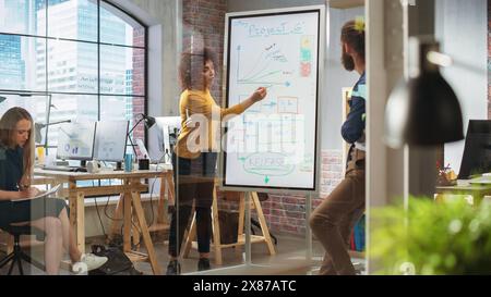 Motivierte, visionäre Geschäftsfrau, die ein Team-Meeting im Konferenzraum „Creative Office“ leitet. Aufgeregt multiethnische Frau zeigt Präsentation auf digitalem Whiteboard-Monitor. Stockfoto