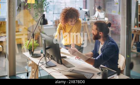 Zwei stilvolle Mitarbeiter diskutieren über arbeitsbezogene Projekte am Computer in Creative Agency in Loft Office. Junger kreativer Mann und Frau, der über ein Unternehmensprojekt spricht Stockfoto