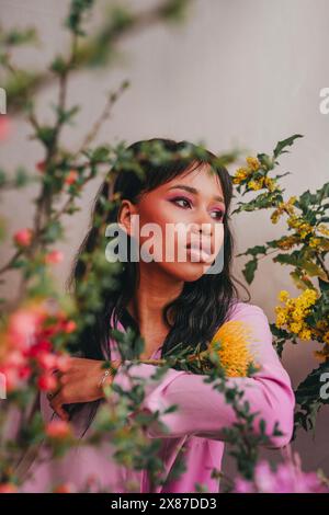 Nachdenkliche junge Frau inmitten farbenfroher Blumen Stockfoto