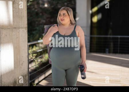 Kurvige junge Frau mit einer Wasserflasche, die auf der Fußgängerbrücke steht Stockfoto