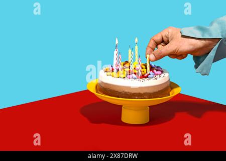 Hand des Mannes, die Kerze auf Schokolade und Vanille Geburtstagskuchen vor blauem Hintergrund setzt Stockfoto