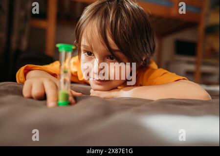 Nachdenklicher Junge, der zu Hause auf Sanduhr schaut Stockfoto