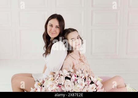 Lächelnde Frau, die Rücken an Rücken mit Tochter vor der Wand sitzt Stockfoto