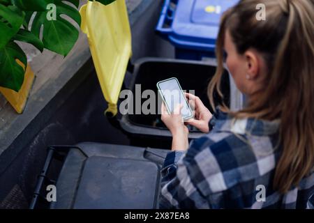 Reife Frau, die ihr Handy in der Nähe von Mülltonnen benutzt Stockfoto