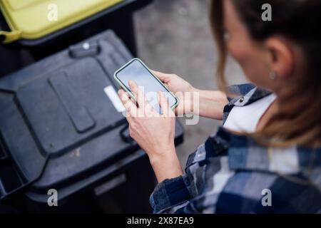 Reife Frau, die ihr Smartphone in der Nähe von Mülltonnen benutzt Stockfoto