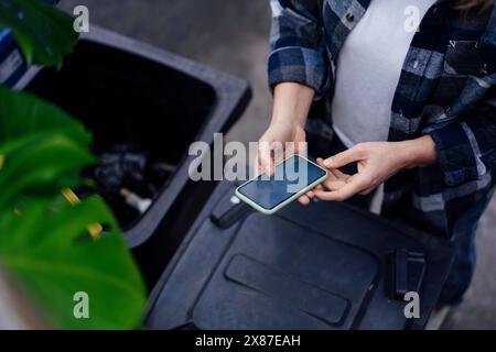 Reife Frau, die ihr Handy in der Nähe des Mülltonnen benutzt Stockfoto