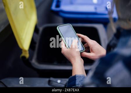 Reife Frau, die ihr Smartphone in der Nähe des Mülltonnen benutzt Stockfoto