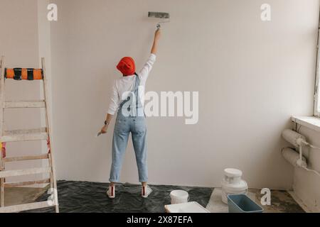 Frau, die Malerwalze an der weißen Wand in einem neuen Zuhause benutzt Stockfoto