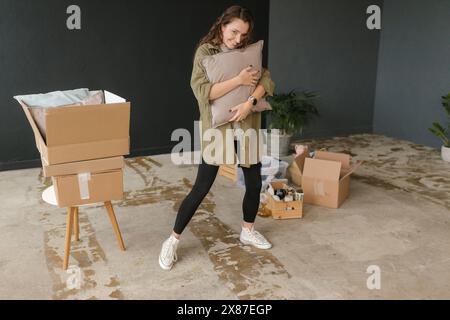 Glückliche Frau umarmt Kissen zwischen Pappkartons in einem neuen Zuhause Stockfoto