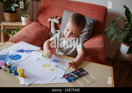Junge, der zu Hause Handabdrücke auf Blatt Papier macht Stockfoto