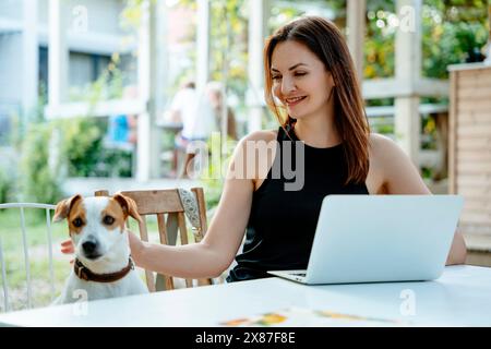 Lächelnde Frau, die mit Laptop sitzt und Jack Russell Terrierhund im Hinterhof ansieht Stockfoto
