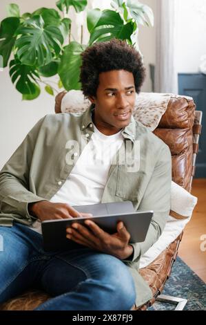 Lächelnder Geschäftsmann, der sich auf einem Liegestuhl mit einem Laptop zurücklehnt und zu Hause arbeitet Stockfoto